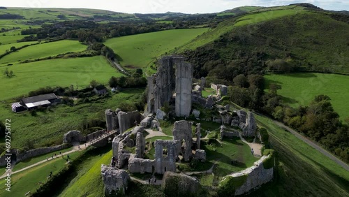 Aerial shot ruins of Corfe Castle on hill with scenery passing in the background on autumn day. Top cinematic aerial view. United Kingdom aerial.  photo