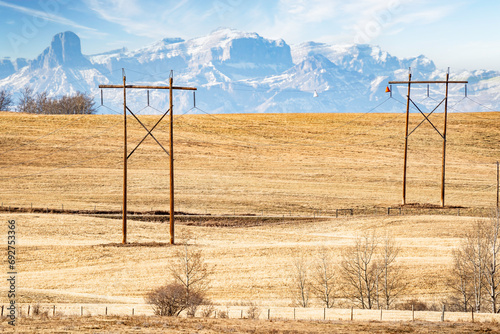 Pair of large wooden power poles with hanging electrical wires overlooking a hilltop and the distant Canadian Rocky Mountains near Cochrane Alberta Canada. photo