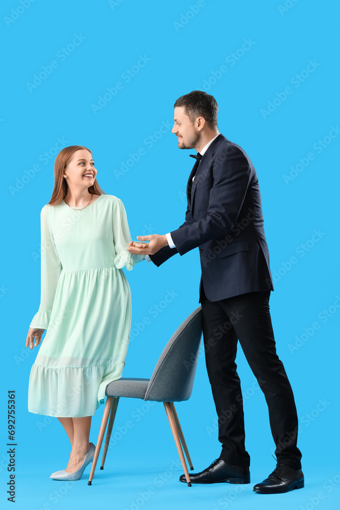 Obraz premium Young man offering his wife to sit in chair on blue background