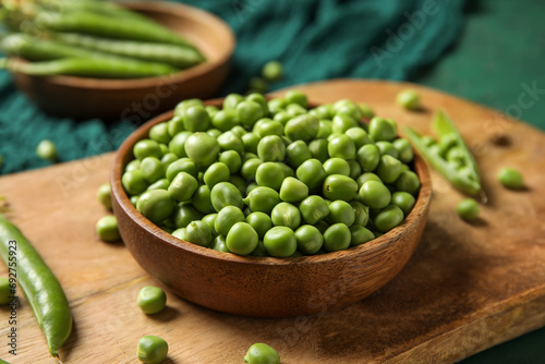 Bowl and wooden board with fresh green peas on color background, closeup