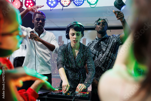 Dj and singers band energetic performance on stage at nightclub disco party. Energetic african american men musicians and caucasian frontwoman playing electronic music live at discotheque photo