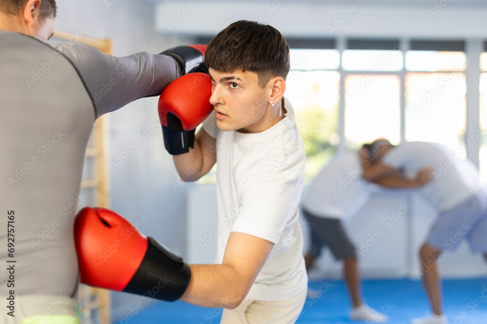 Two men in group boxing classes practicing sparring technique of blowing to body in gym