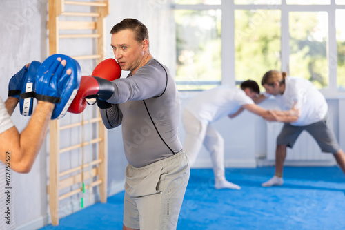 Focused man in boxing gloves practices punches with man in mitts in gym © JackF