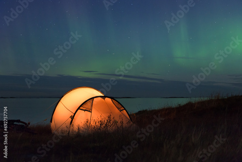 Northern lights dancing over an iluminated tent at the Atlantic coast in Norway © Alexander Erdbeer