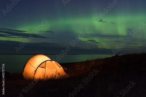 Northern lights dancing over an iluminated tent at the Atlantic coast in Norway photo