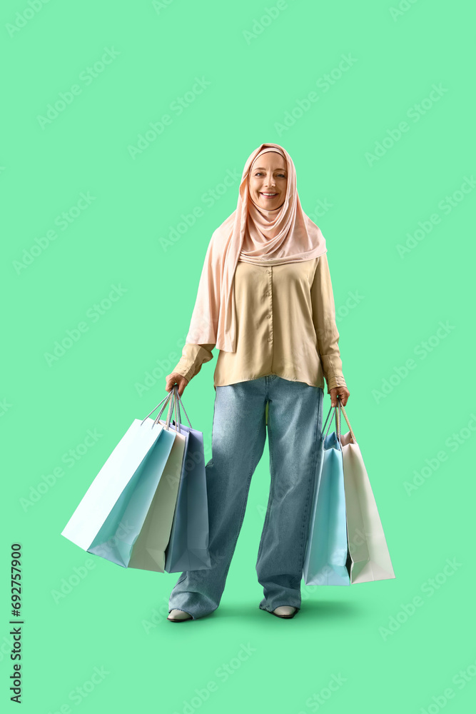 Mature Muslim woman with shopping bags on green background Mature Muslim woman with shopping bags on green background