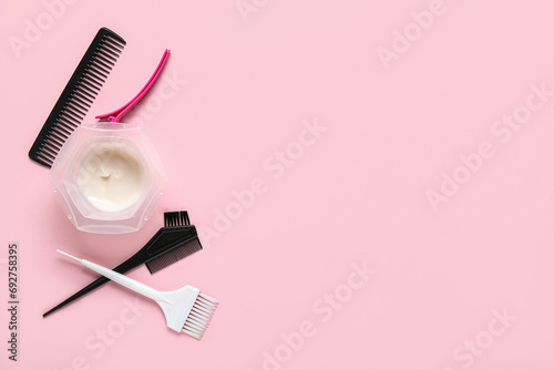 Bowl with hair dye, combs and brushes on pink background photo