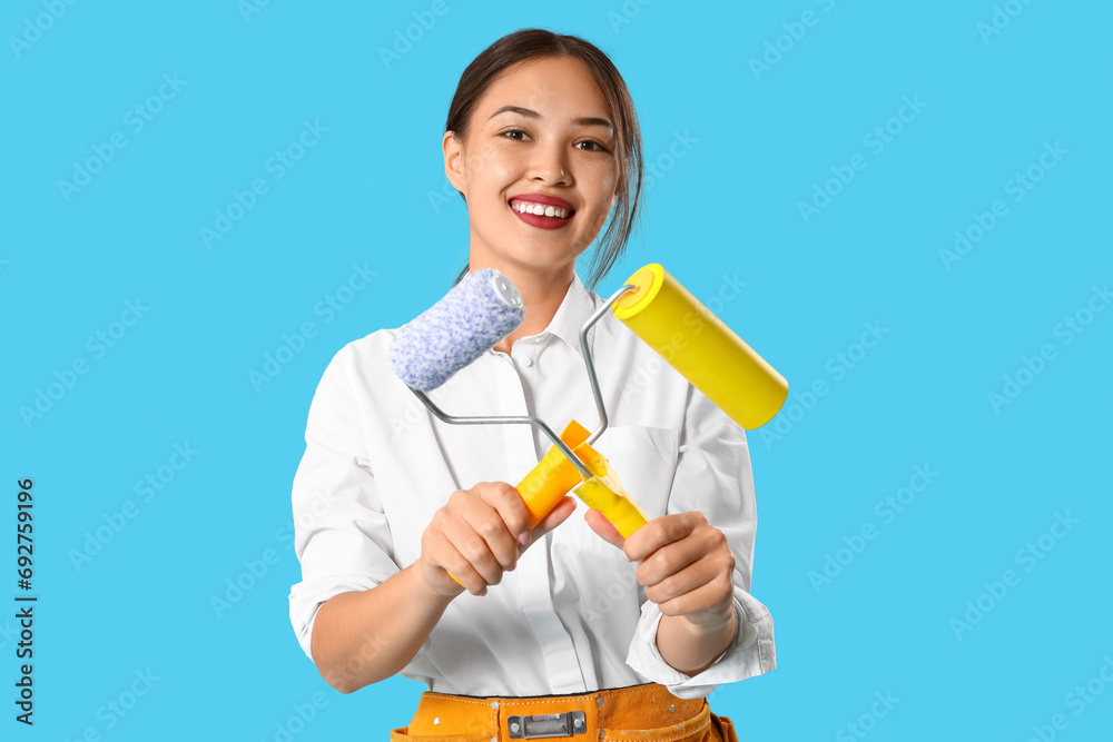 Female Asian decorator with paint rollers on blue background Female Asian decorator with paint rollers on blue background
