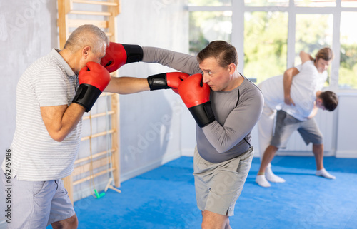 Adult man with partner in boxing gloves boxing in gym..