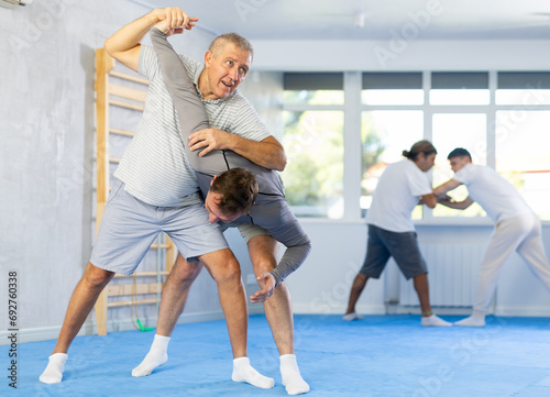 Adult man and elderly men judokas practicing judo technique in gym.. © JackF
