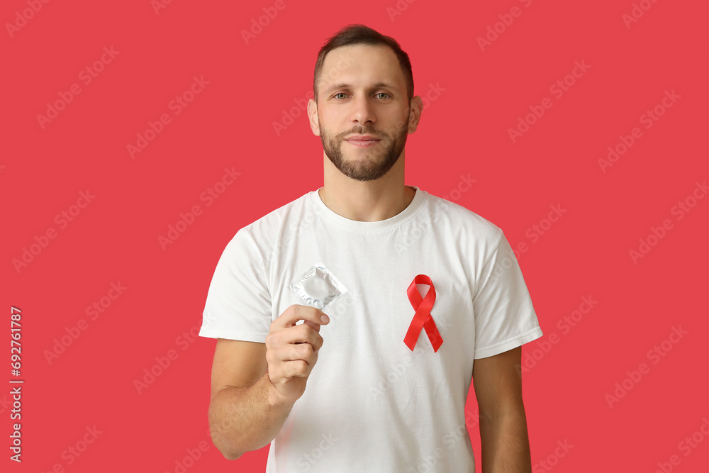 Young man with red ribbon and condom on color background. AID awareness concept Young man with red ribbon and condom on color background. AID awareness concept