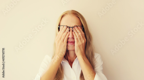 Tired overworked middle-aged woman employee rubbing her eyes suffering from eye strain, dry eye syndrome or headaches after working at the computer for a long time. Exhausted office worker photo