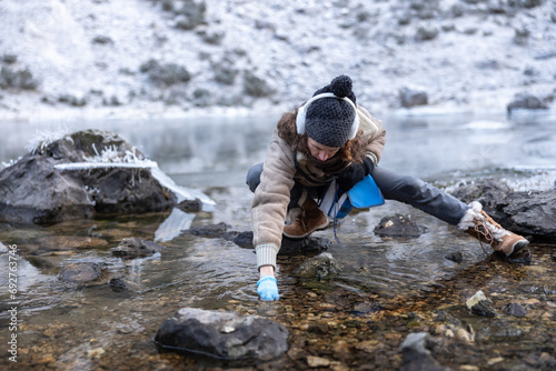 Woman Biologist Collecting Environment Samples from a Mountain Lake in Winter photo