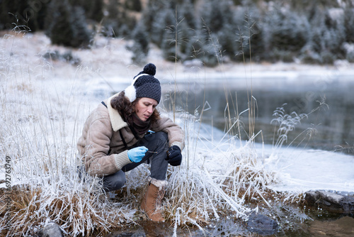 Female Environment Researcher Examining Presence of Algae in Squatting Position near a Frozen Mountain Lake