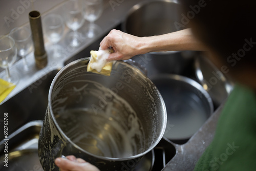 Adult Woman Washes Cooking Pots by Hand in a Restaurant Kitchen Close Up Over the Shoulder View