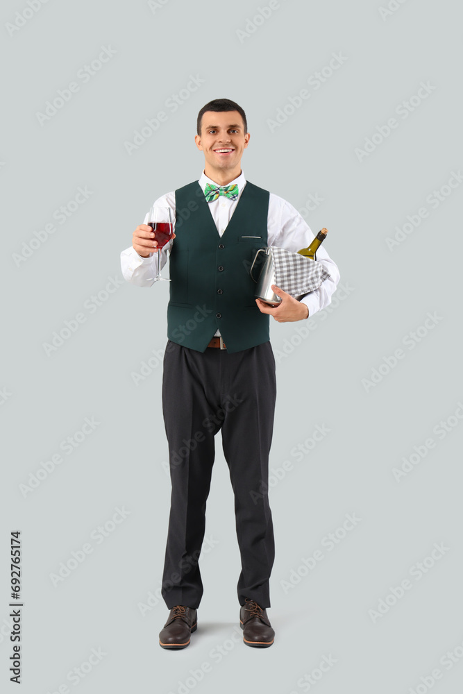 Young waiter with wine on grey background Young waiter with wine on grey background