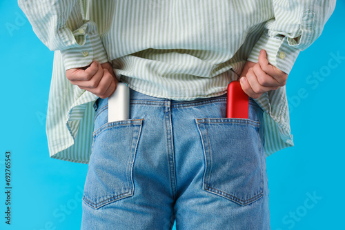 Young man with electronic cigarettes in pockets on blue background, closeup