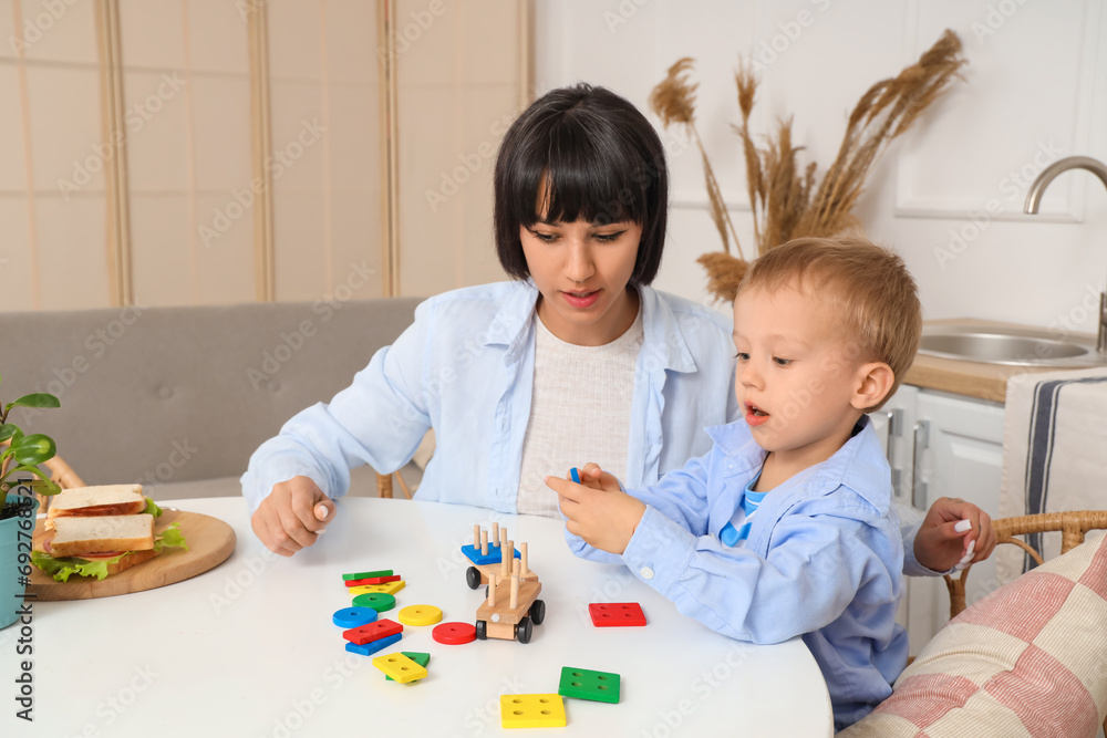 Young mother and her little son playing with building blocks at table in kitchen Young mother and her little son playing with building blocks at table in kitchen