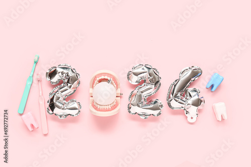 Composition with figure 2024 made of foil balloons, jaw model and toothbrushes on pink background