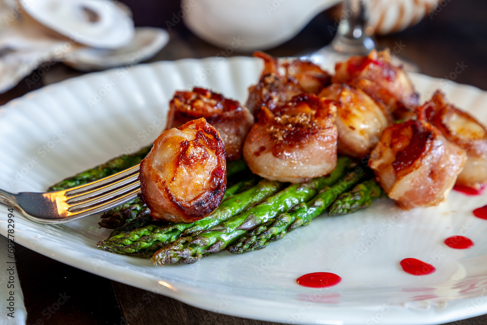 Candied bacon wrapped sea scallops over a bed of asparagus on fine China Candied bacon wrapped sea scallops over a bed of asparagus on fine China