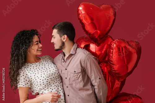 Young couple with air balloons in shape of heart for Valentine's day on red background