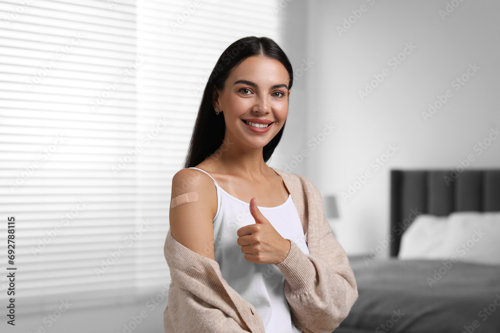 Woman with sticking plaster on arm after vaccination showing thumbs up in bedroom Woman with sticking plaster on arm after vaccination showing thumbs up in bedroom