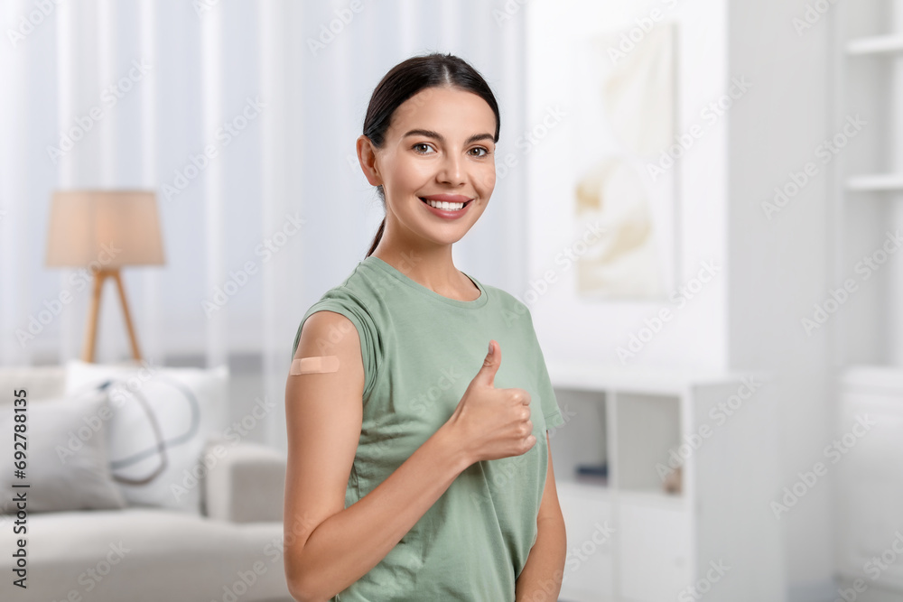 Woman with sticking plaster on arm after vaccination showing thumbs up at home Woman with sticking plaster on arm after vaccination showing thumbs up at home