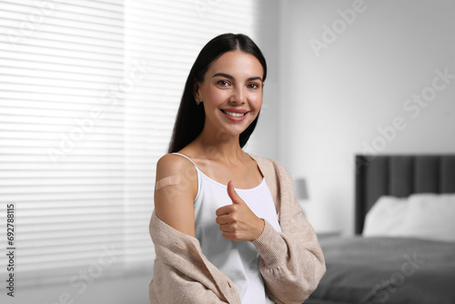 Woman with sticking plaster on arm after vaccination showing thumbs up in bedroom