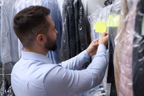 Dry-cleaning service. Worker sticking paper note onto clothes indoors