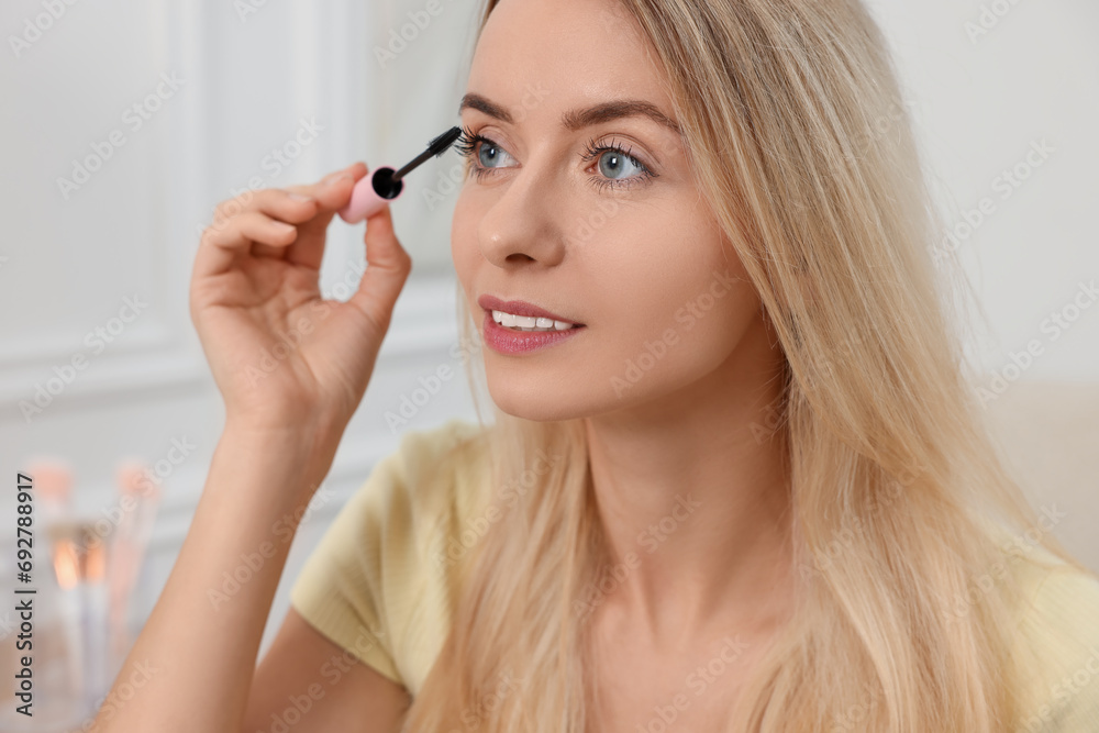 Beautiful woman applying mascara with brush indoors, closeup Beautiful woman applying mascara with brush indoors, closeup