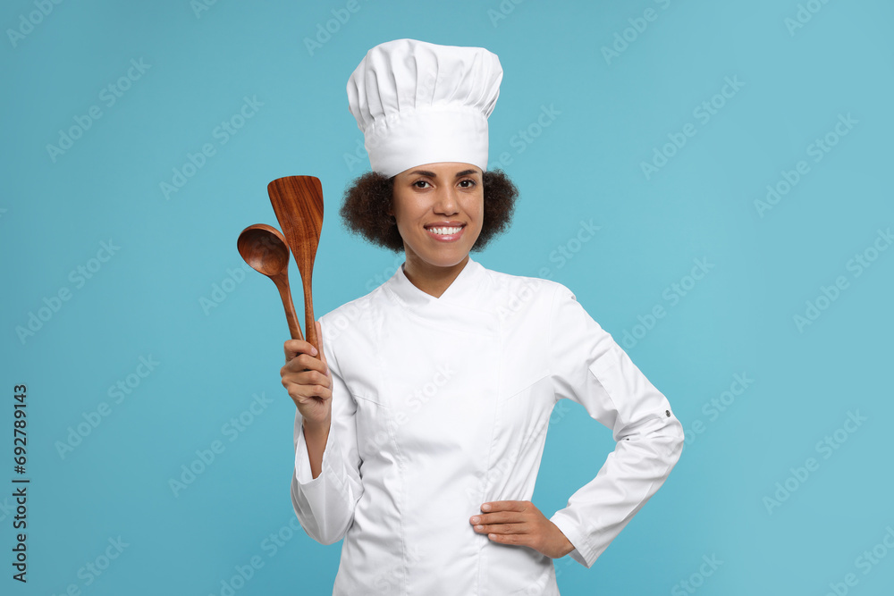Naklejka premium Happy female chef in uniform holding spoon and spatula on light blue background