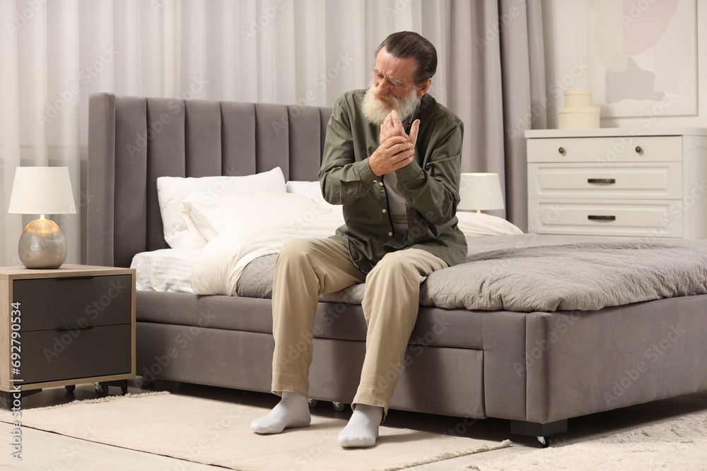 Fototapeta premium Senior man suffering from pain in hand on bed at home. Rheumatism symptom
