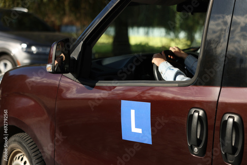 Learner driver driving car with L-plate, view from outside. Driving school