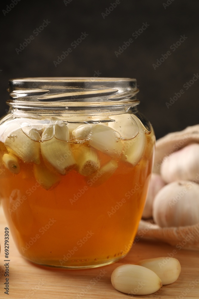 Honey with garlic in glass jar on wooden table, closeup