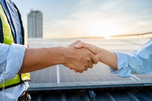 Two Electrical Engineers shaking hands after working to inspect the installation and maintenance of solar panels in the solar power station, Renewable Energy, sustainable business concept.