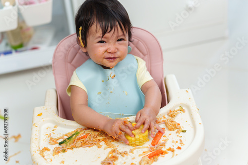 happy infant baby eating food and vegetable by self feeding BLW or baby led weaning on chair photo