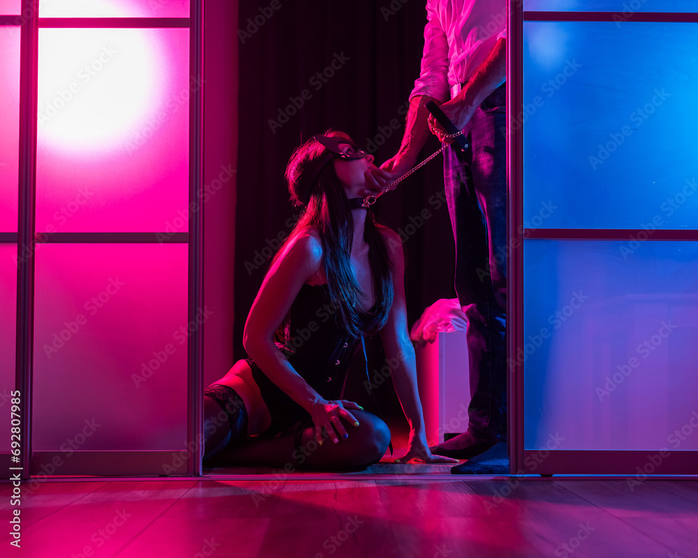A woman is kneeling in front of a man. BDSM sex concept. Vertical photo.  - obrazy, fototapety, plakaty 