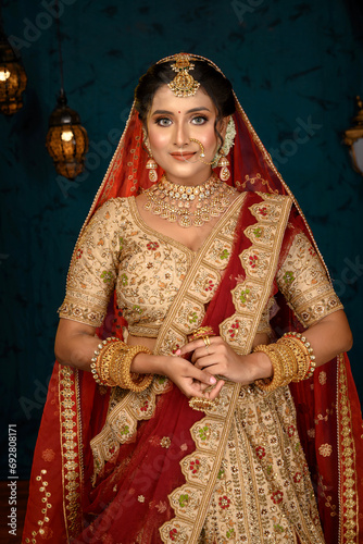 Stunning Indian bride dressed in traditional bridal lehenga with heavy gold jewellery and veil posing fashionable in studio lighting