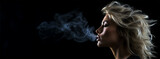a young blonde woman exhales with pleasure Cigarette smoke on a dark background, the concept of health care and the harm of smoking. banner, free space for text. 