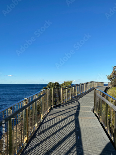 Boardwalk to the beach. Wooden bridge over the sea. Walkway near the blue turquoise ocean, waves. Pier in the sea. Wood fence.