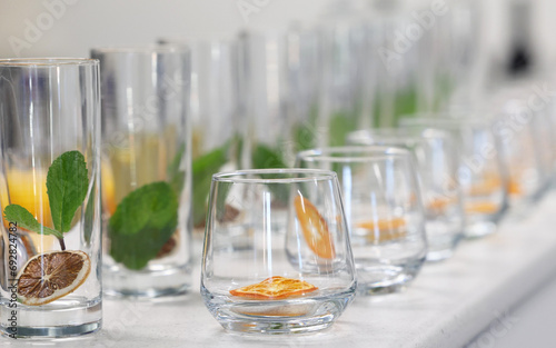 Clean glass tumblers or drinking glasses with dried dehydrated citrus fruit slices inside with mint leaves ready for a cocktail or mocktail to be poured in.