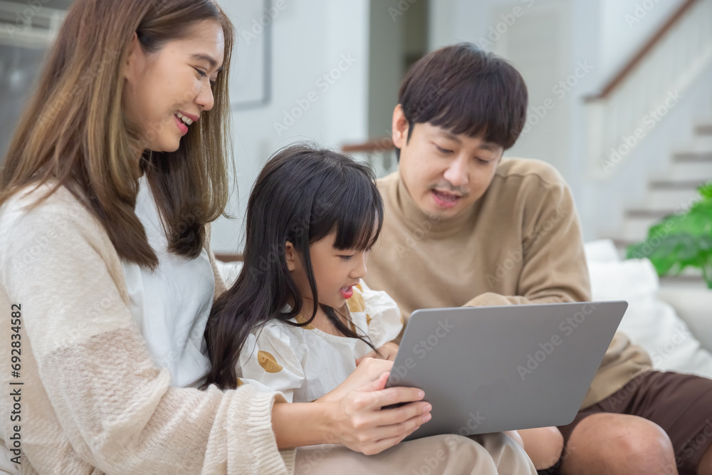 Happy asian family father mother and child daughter having fun using laptop computer sitting on couch in living room at home. Parents teach child girls computer skills learning browsing internet. Happy asian family father mother and child daughter having fun using laptop computer sitting on couch in living room at home. Parents teach child girls computer skills learning browsing internet.