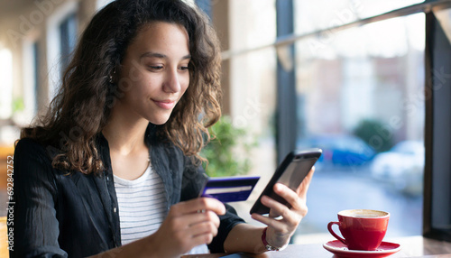 Young woman holding credit card and using mobile phone in cafe. Online shopping concept