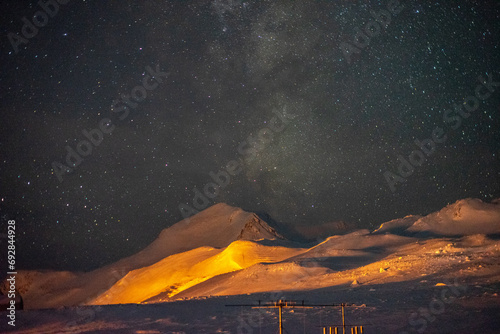 The Milky Way visible over the yellow-lit mountains of Antarctica photo