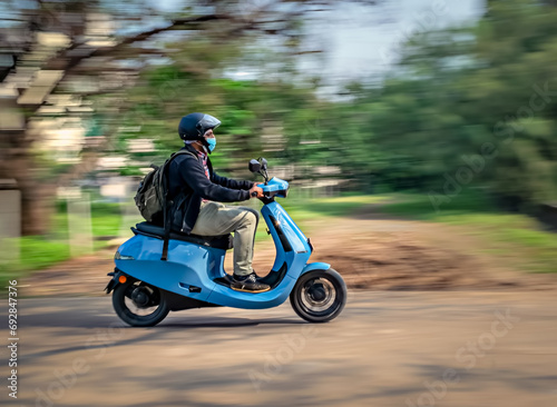 Slow shutter, Motion blur image of a rider wearing helmet for safety, riding on a blue electric moped. photo