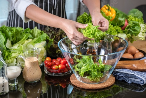 woman chef mix fresh baby cos salad and pour salad dressing in glass blow. Organic Vegetables mix all green salad In glass bowl. Breakfast fresh salad and clean vegetable.