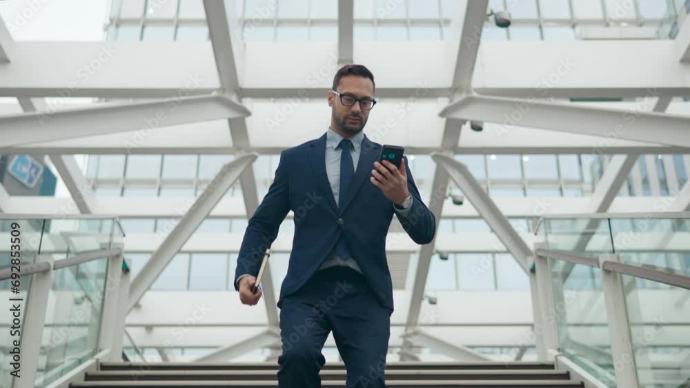 Businessman rushes down staircase holding notebook reads message on phone on the go Businessman rushes down staircase holding notebook reads message on phone on the go