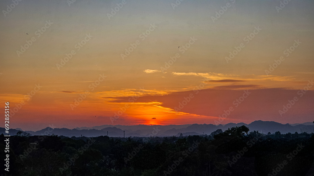Beautiful sunset in the mountains. Sunset with beautiful orange evening sky and silhouette of trees. Dramatic sunrise