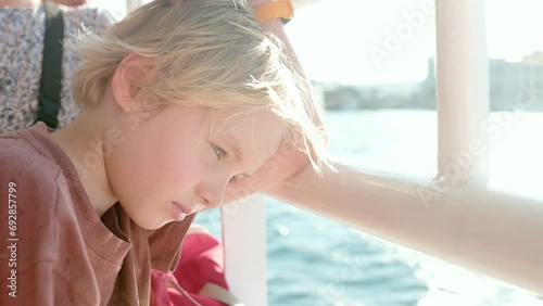 Blonde preteen boy is traveling by boat or ferry on the sea. Family vacations on ocean or sea. Summer leisure for families with kids. Child overheated on a hot sunny day. Bored child on holiday trip photo