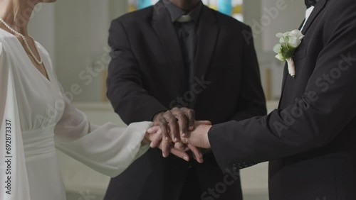 Tilt down slowmo of Caucasian mature couple looking at each other with love and tender while being pronounced husband and wife by young Black male officiant putting his hand on theirs